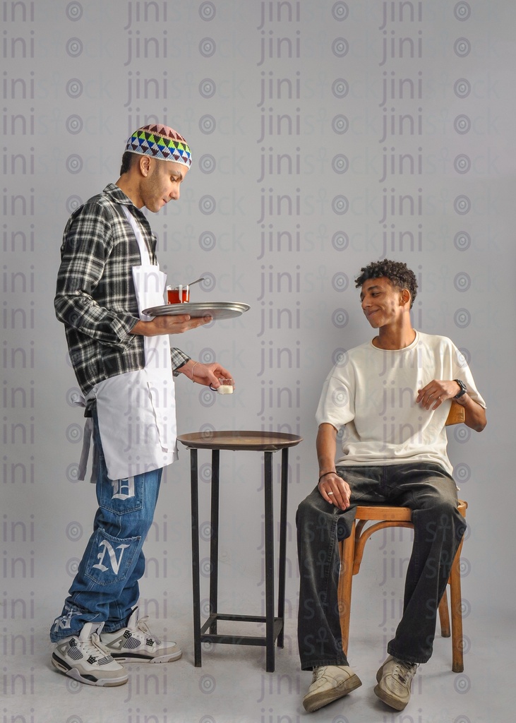 a waiter holding a tray of tea and holding the sugar in his hand giving them to a customer in a coffee shop or café. the waiter wearing the work clothes