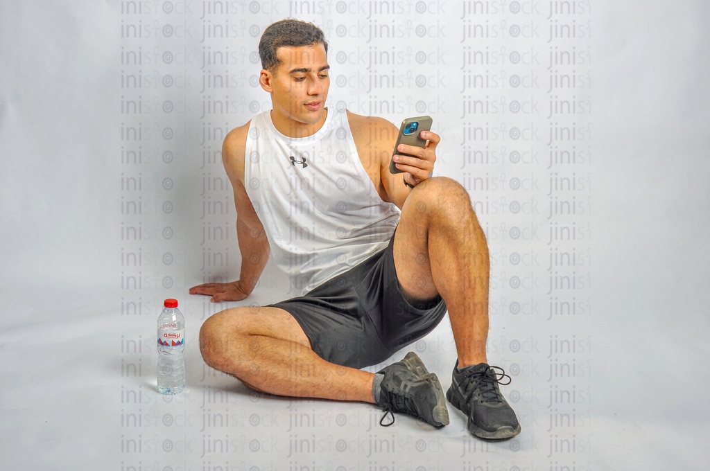 an athlete man sitting on the land holding a mobile phone and texting
