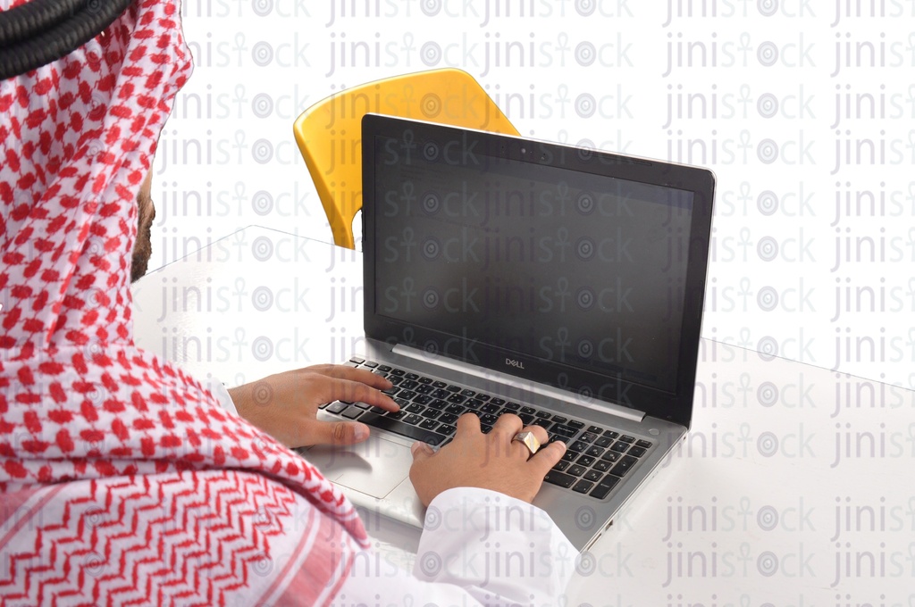 over-shoulder shot of a Saudi, Khaliji,  Emirati or a man from the Gulf working on a laptop in his office.
