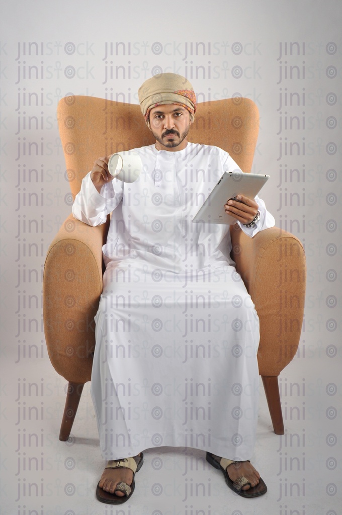 رجل عماني من الخليج يرتدي الزي العماني أنهى قهوته وهو جالس على كرسي