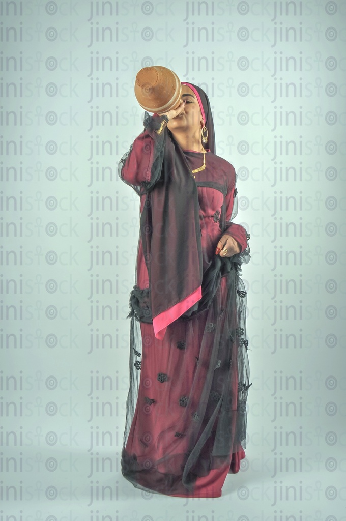 An Egyptian farmer girl or a Nubian Egyptian woman wearing Nubian clothes or a lady farmer drinking water from Qola