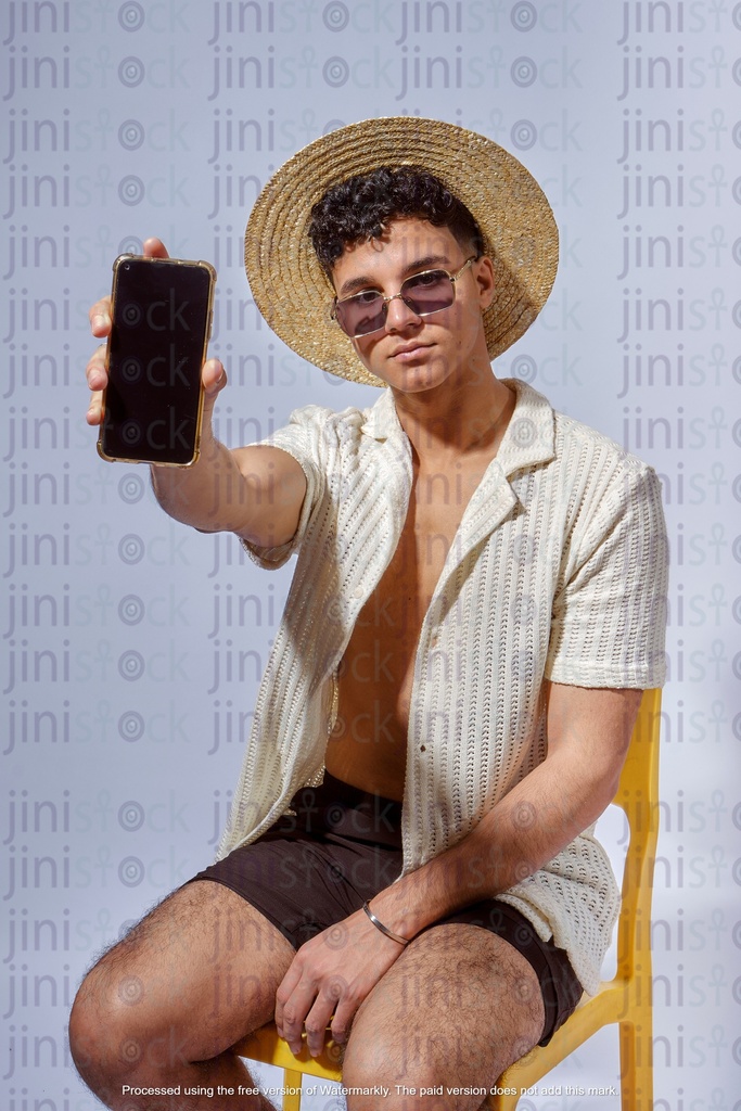 young egyptian man holding mobile while wearing a hat and sun glass in summer outfit