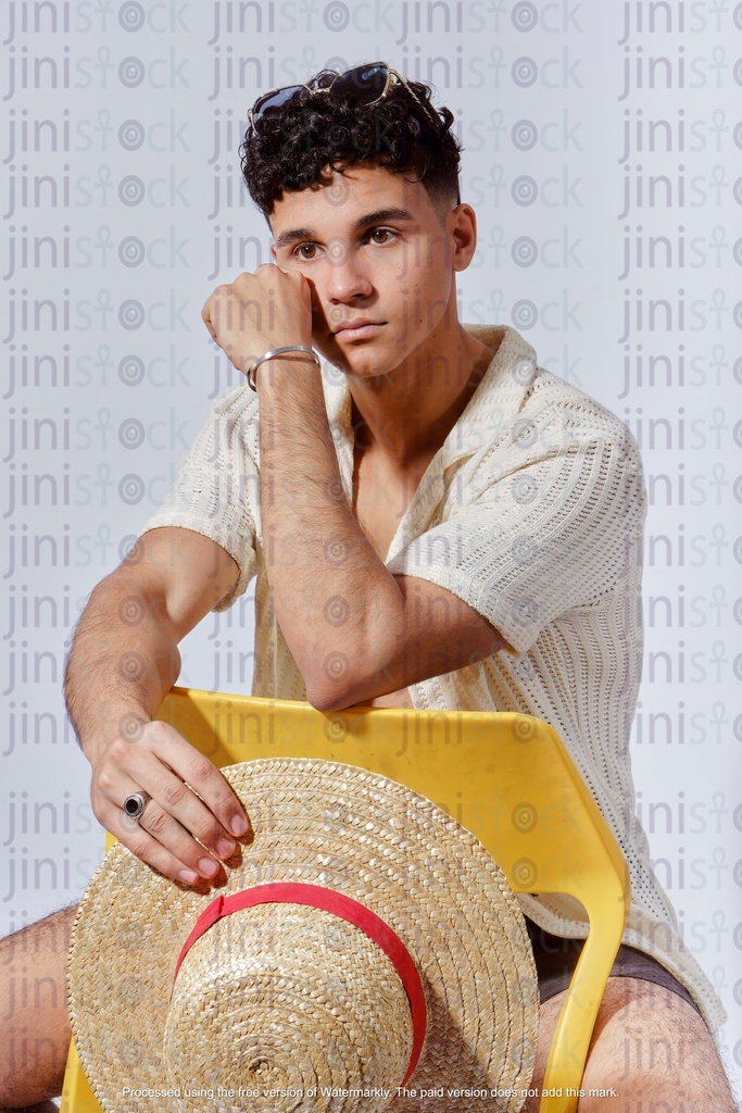 young egyptian man sitting on the chair in backwards and holding a summer hat