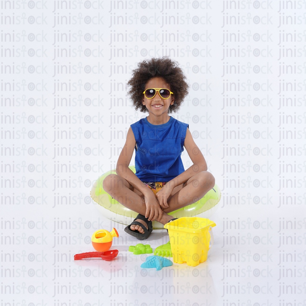 young Egyptian boy with curly hair  in summer cloth playing on the beach with toys and wearing sunglass