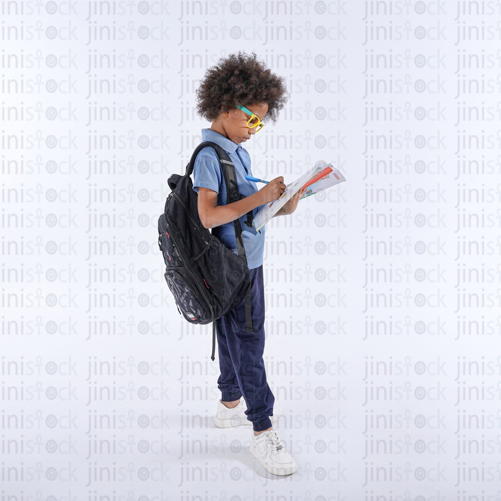 liittle student boy carrying his bag and writting something in his book studying