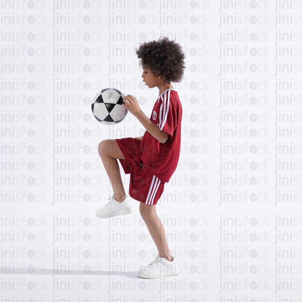 Qatar boy with curly hair wearing qatar national football team and kicking football