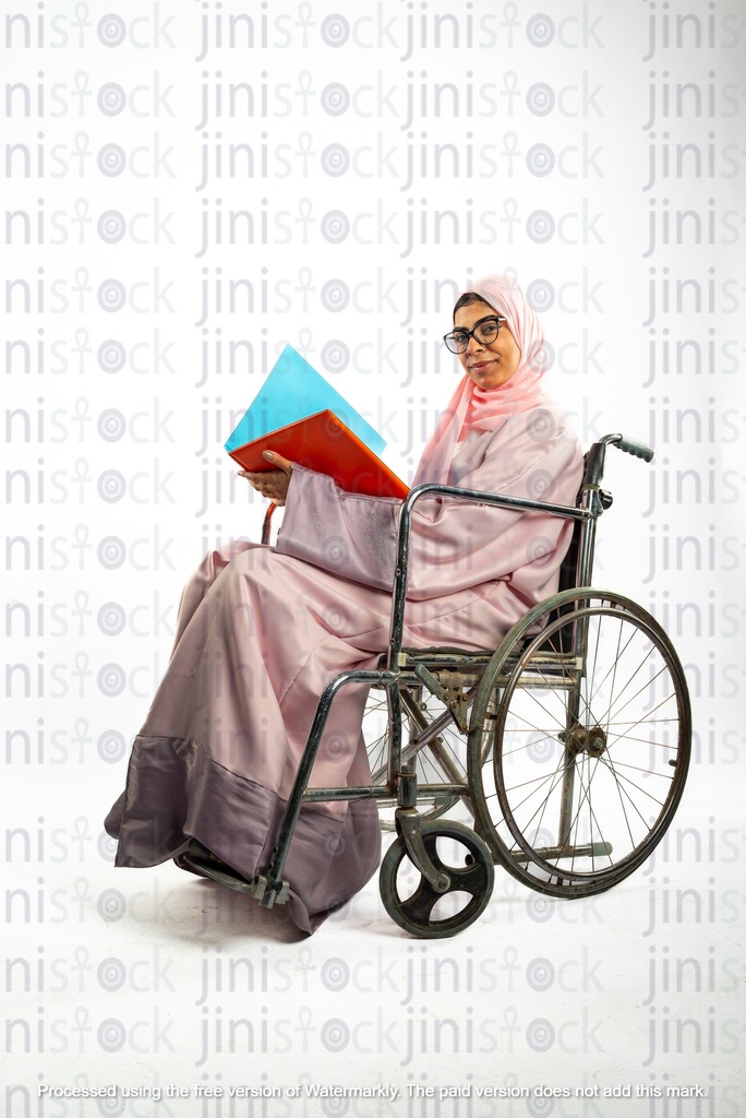 امرأة خليجية سعودية من الخليج على كرسي متحرك وتعاني من إعاقة، تنظر إلى الكاميرا وهي تحمل ملف عمل.