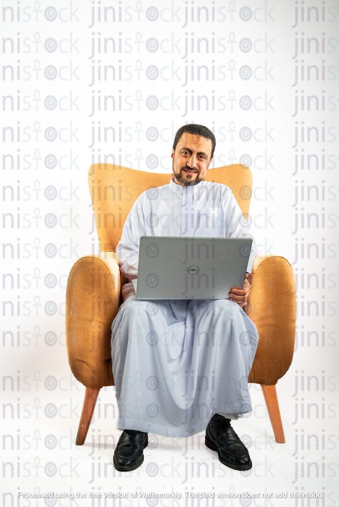 رجل سعودي خليجي من الخليج يجلس على كرسي ويعمل على الكمبيوتر المحمول الخاص به