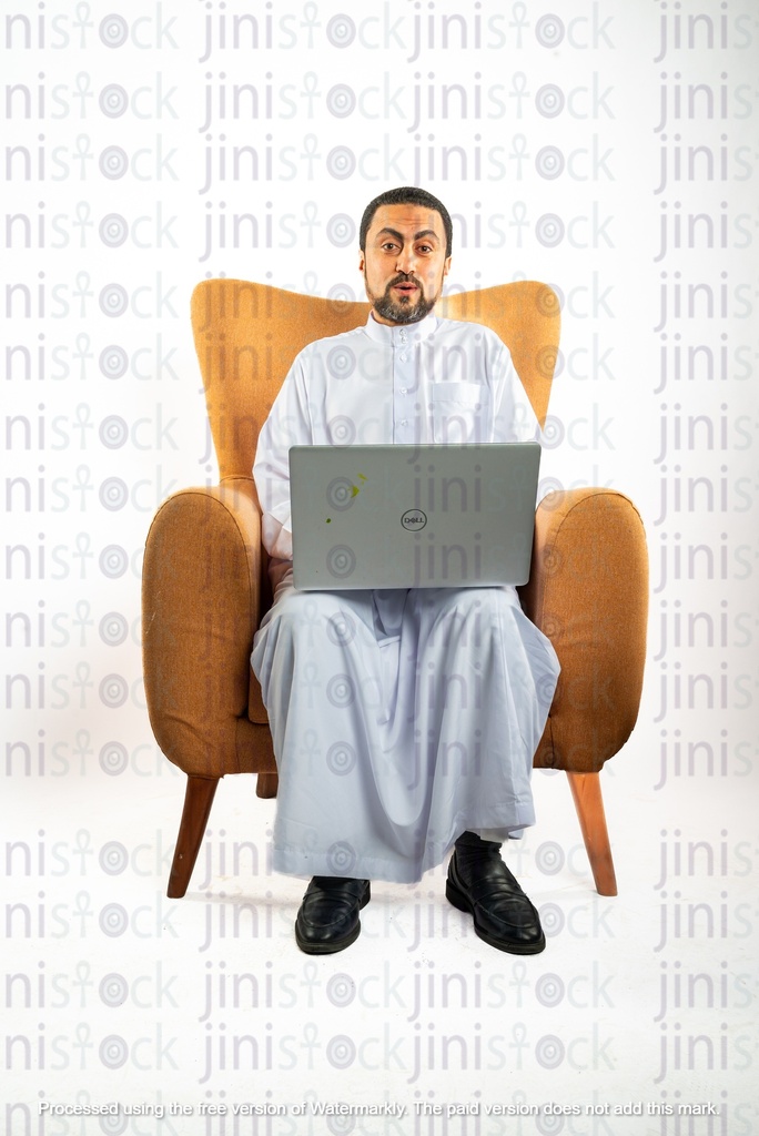 رجل سعودي خليجي من الخليج يجلس على كرسي يعمل على الكمبيوتر المحمول الخاص به وهو متفاجئ