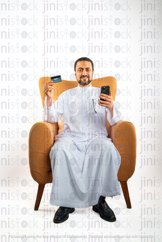 saudi khaliji man from gulf sitting on a chair holding mobile phone in one hand and a visa card on the other