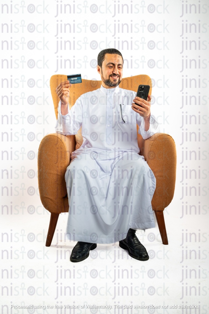 saudi khaliji man sitting on the chair holding a credit card and mobile phone