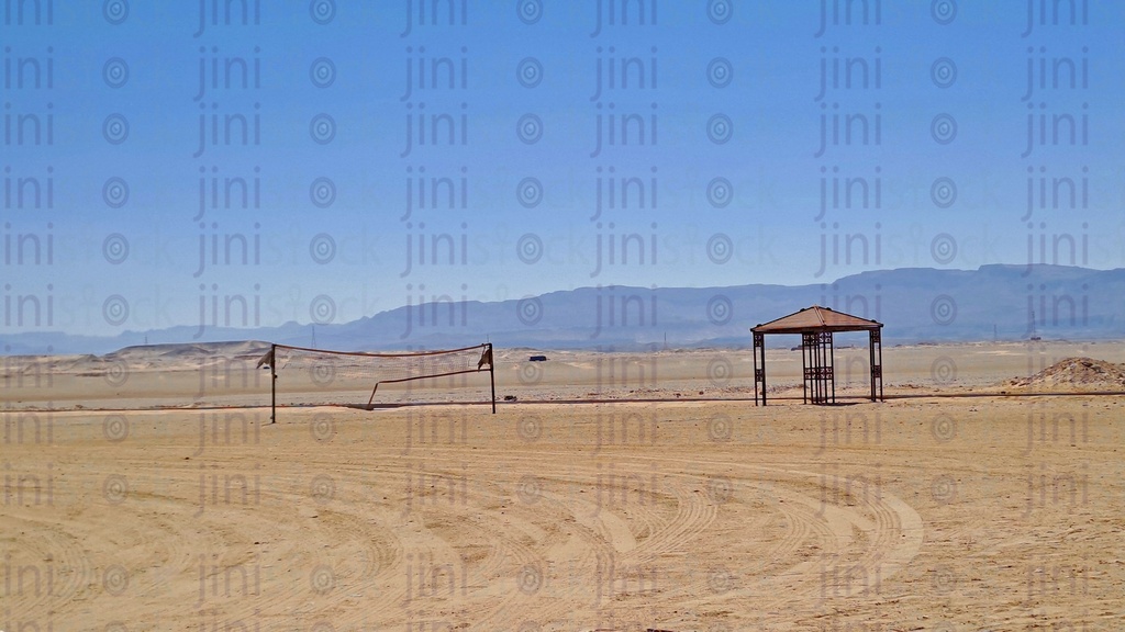 Golden-colored sands in the desert with an umbrella ,a net for handball and mountains- as background for designs.