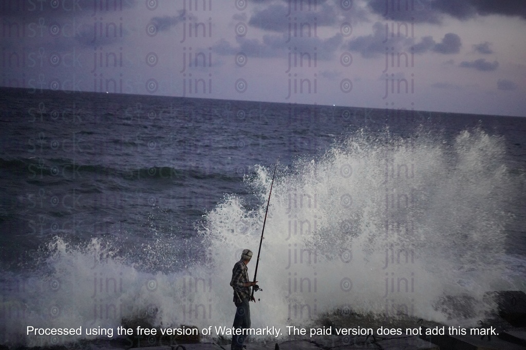 fisherman standing on the rocks facing the waves