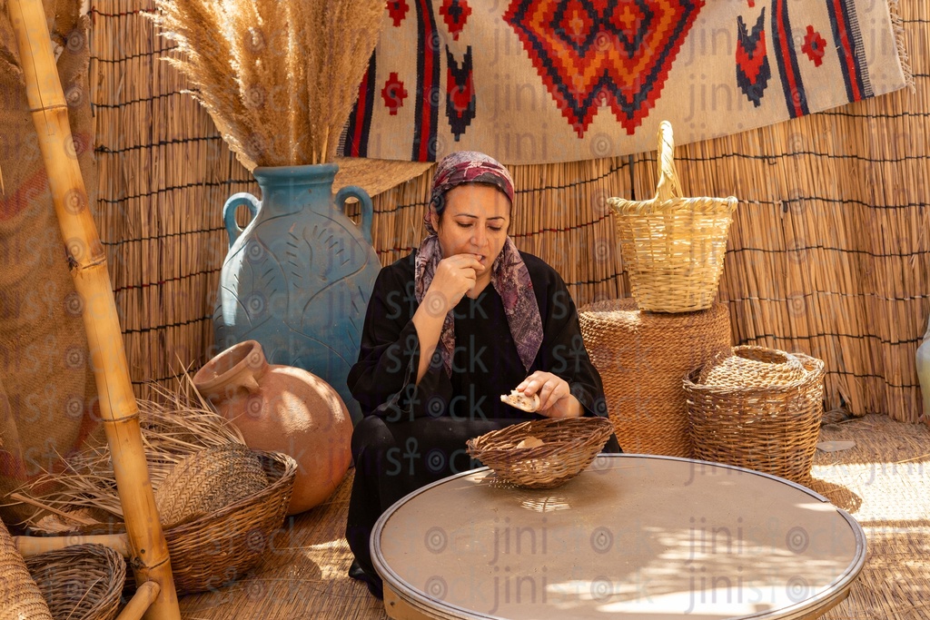 A woman sitting and eating bread in a straw hut