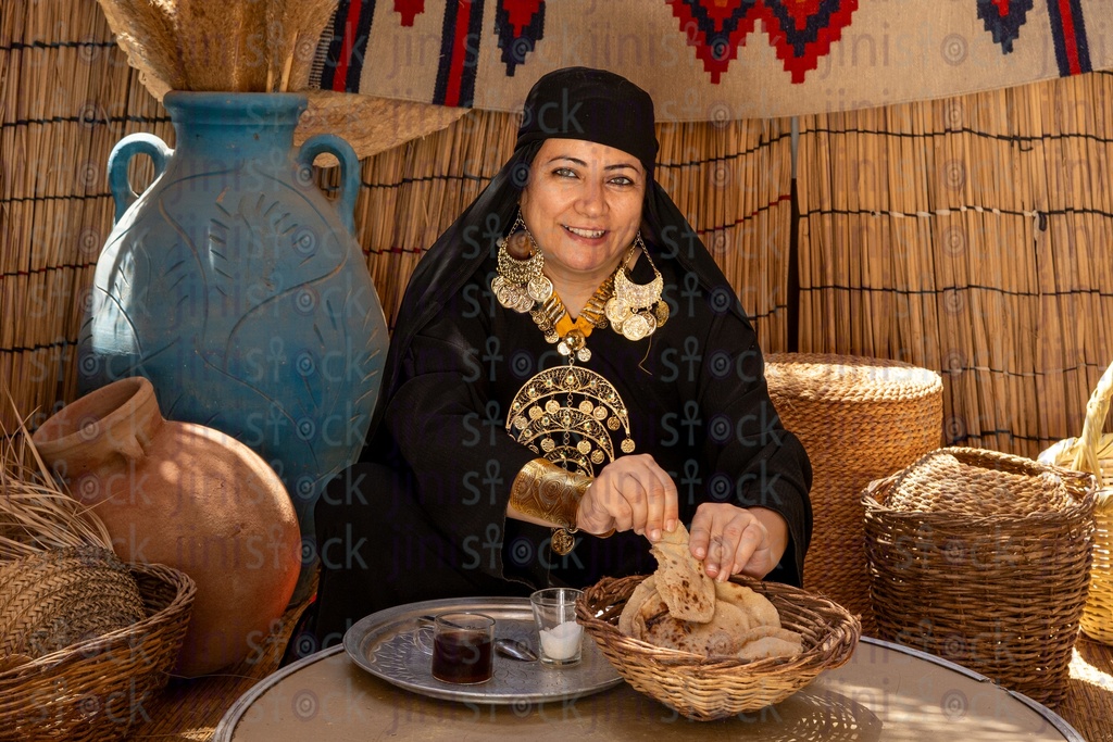 Bedouin woman eating a loaf of local bread with a cup of tea next to her 