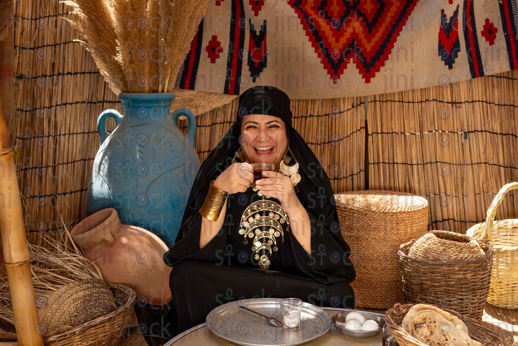 A laughing Bedouin woman drinking tea and having breakfast next to her