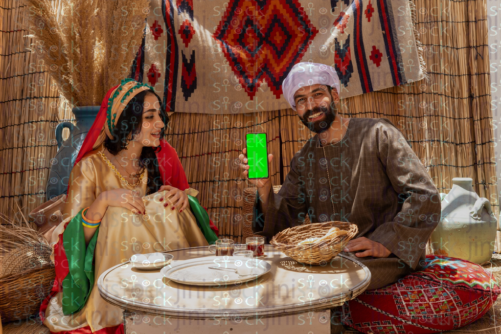 A young man is sitting holding a phone with a green screen and a young woman is sitting next to him