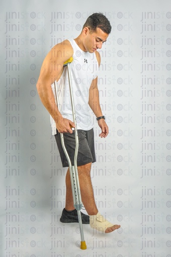 An athlete man has a foot injury and walking with a crutch side view