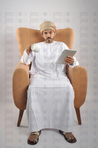 رجل عماني من الخليج يرتدي الزي العماني أنهى قهوته وهو جالس على كرسي