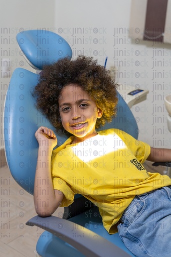 A boy sitting on the dental chair waiting for a dental care the boy is with curly hair