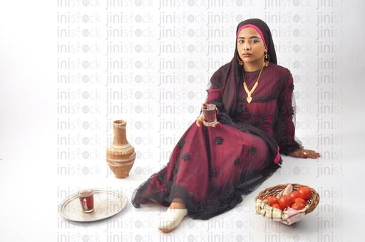 A Nubian Egyptian woman wearing a Nubian dress, a veil on her head, sitting on the land, and drinking a cup of tea