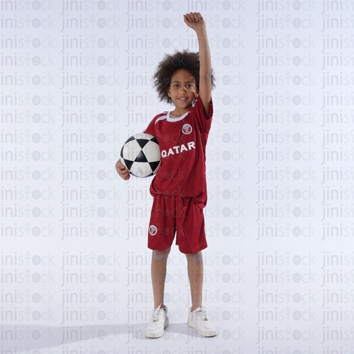 little boy wearing qatar national football shirt and holding a football and cheering