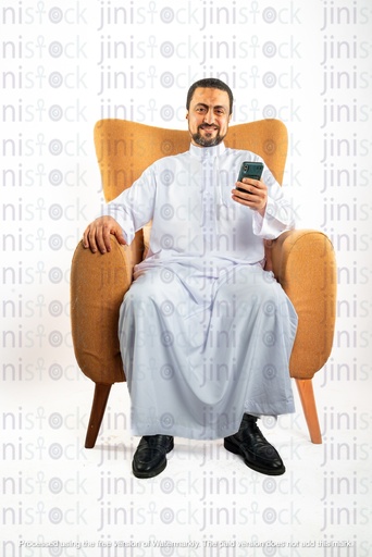 رجل سعودي خليجي يجلس على الكرسي ويتحقق من هاتفه المحمول