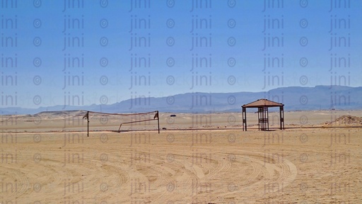 Golden-colored sands in the desert with an umbrella ,a net for handball and mountains- as background for designs.