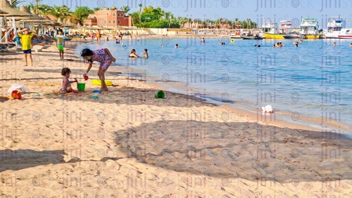a beach in Hurghada where people swimming and kids playing with the sand