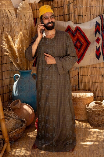 An Egyptian farmer stands happy talking on the phone wearing a galabiya 