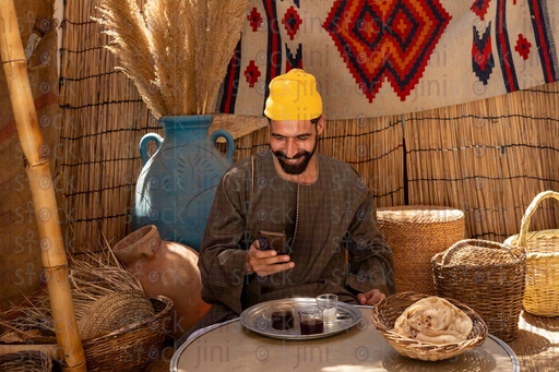 رجل مصري ممسك بهاتفه مبتسما جالس في كوخ