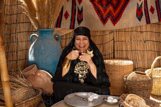 A laughing Bedouin woman drinking tea and having breakfast next to her