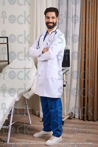 An Egyptian doctor standing in his clinic, smiling, wearing a medical coat and a stethoscope