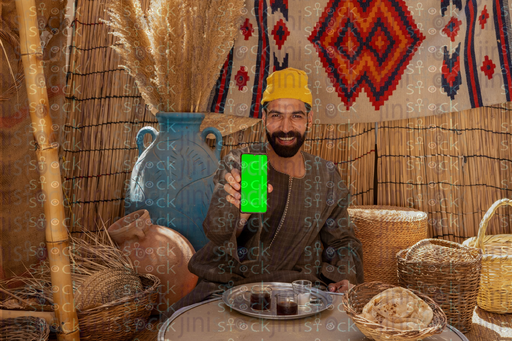 Egyptian man sitting holding a phone with a green screen