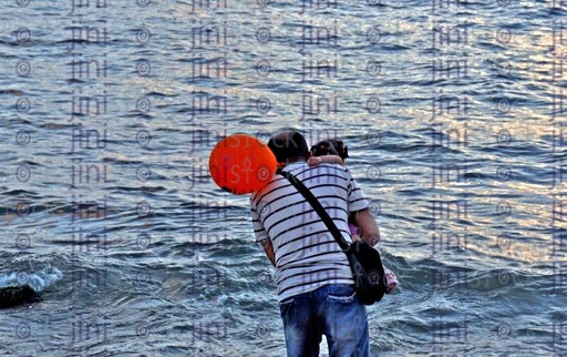 A man on the beach holding his daughter who holding a balloon.